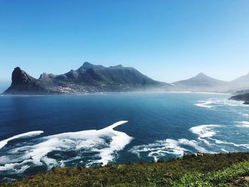 Scenic view of sea and mountains against clear blue sky