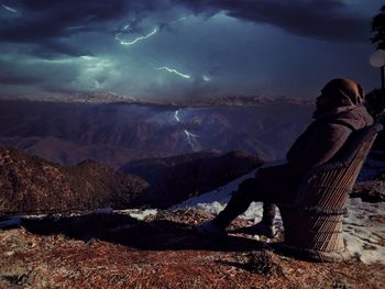 Rear view of man sitting on rock against sky