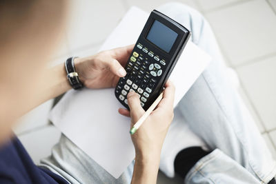 Cropped image of man using calculator while studying at laundromat