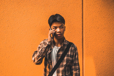 Young man talking on phone while standing by wall