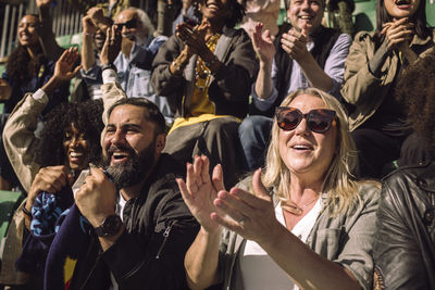 Happy male and female supporters enjoying game from sports stadium stand