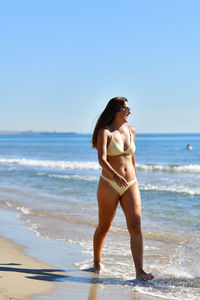 Full length of young woman on beach against clear sky