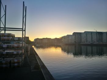 Buildings by river against sky during sunset