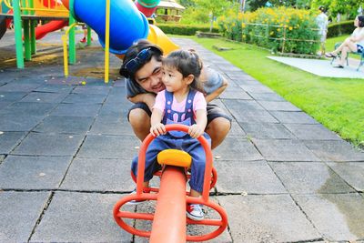 Smiling father playing with daughter sitting seesaw in park