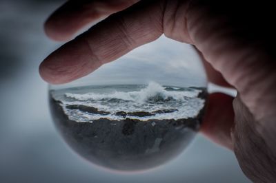 Close-up of human hand holding crystal ball against sea