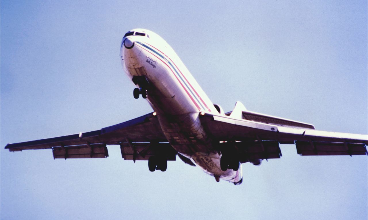 low angle view, clear sky, transportation, mode of transport, blue, airplane, flying, air vehicle, copy space, travel, mid-air, built structure, architecture, on the move, day, outdoors, building exterior, part of, no people, sky