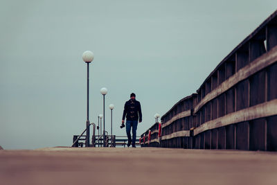 Man with camera walking on road against clear sky