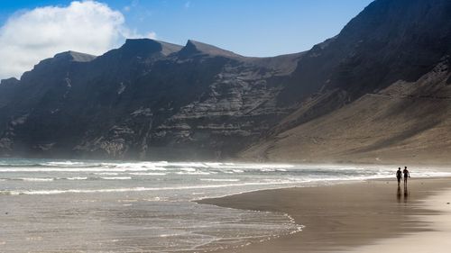 Silhouette friends walking at beach by mountains