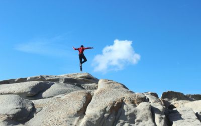 Low angle view of person levitating over rock formation against blue sky