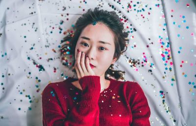 High angle portrait of beautiful young woman lying with confetti on bed at home