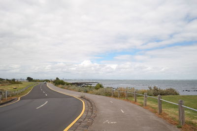 Empty road by sea against sky