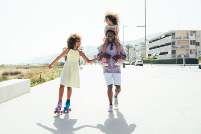 Happy girl roller skating by father carrying sister on shoulders