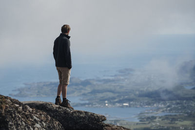 Rear view of man standing on rock against sky