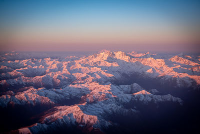 Aerial view of snowcapped mountains against sky during sunset