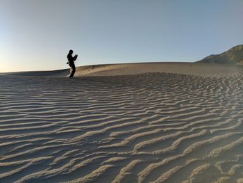 Woman standing at desert against clear sky