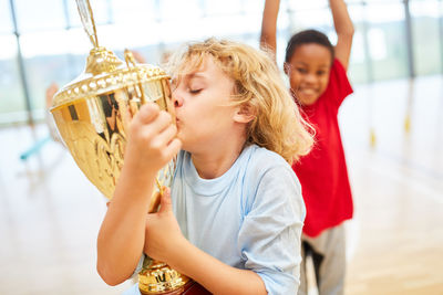 Boy kissing golden trophy while standing in school gym