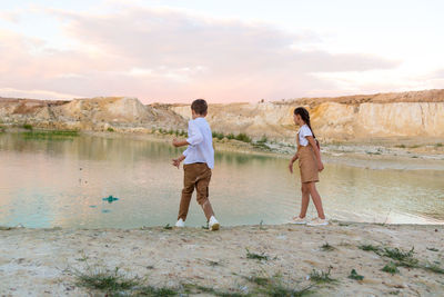 Teenagers 8-9 years old throw stones into the water from the shore, outdoor entertainment together.