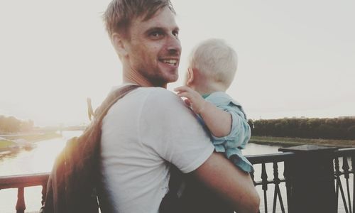 Father and son on railing against clear sky