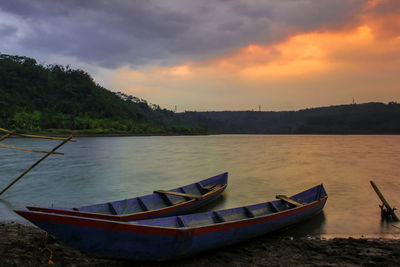 Boat moored on lake against sky during sunset