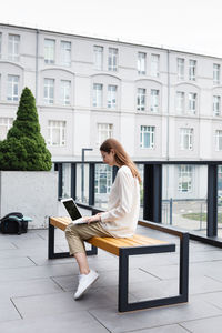 Woman writing and surfing, using laptop sitting college campus