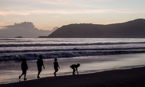 Silhouette people on beach against sky during sunset