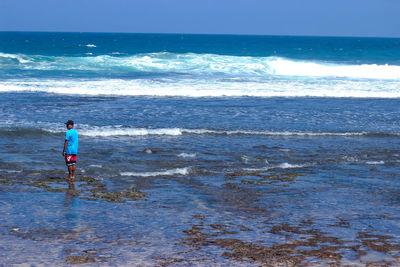 Rear view of man standing at beach against sky