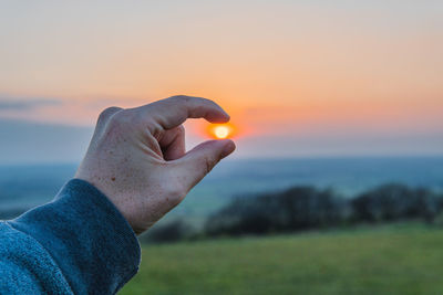 Hand holding the sun during sunset