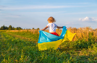 Rear view of woman sitting on field against sky