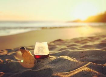 Coffee in glass on sand at beach against sky during sunset