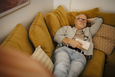 Senior man sleeping with book on sofa at home