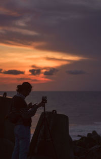 Man using phone at beach during sunset