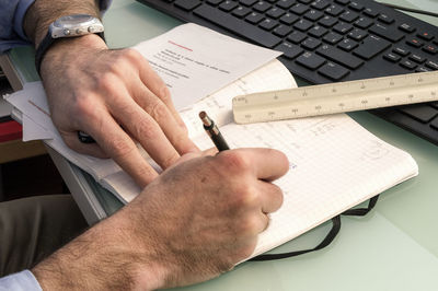 Cropped image of businessman writing in notebook at desk in office