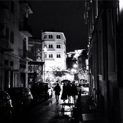 People walking on road along buildings at night