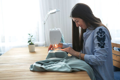 Charming girl with long black hair sews on a sewing machine, concept handmade and mother on 