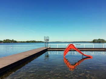 Swimming pool by lake against clear blue sky