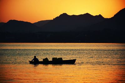 Silhouette boat sailing in lake against orange sky