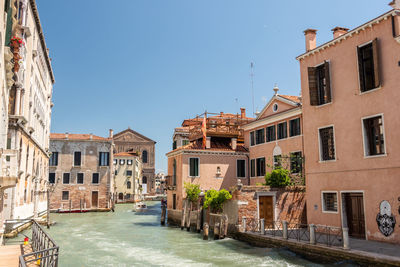 Canal amidst buildings in town against clear blue sky