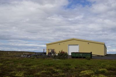 Houses on grassy field against cloudy sky