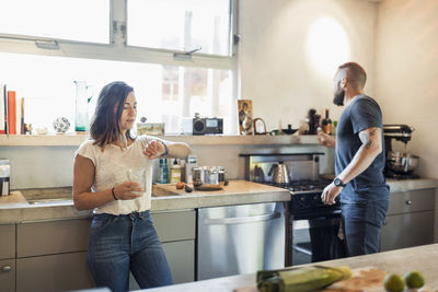 Woman checking time while man looking through window in kitchen