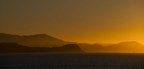 Scenic view of sea against silhouette mountain during sunset
