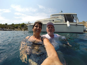 Senior couple taking selfie against yacht in sea