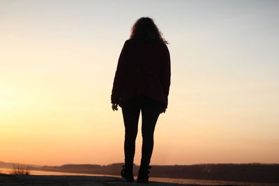 Rear view of silhouette woman standing on beach against sky during sunset