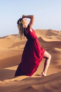 Young woman wearing red dress while standing at desert against clear sky