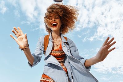 Young woman with arms raised standing against sky