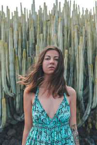 Portrait of beautiful young woman standing against cactus