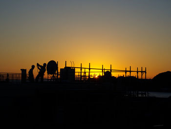 Silhouette workers on building against sky during sunset