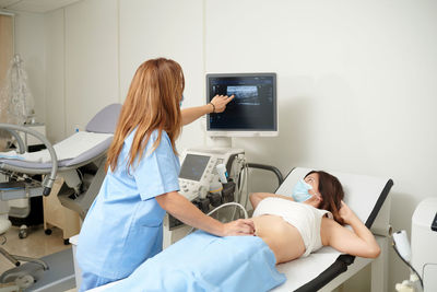 Back view of crop unrecognizable doctor showing video on ultrasound machine display during sonography diagnostic to patient