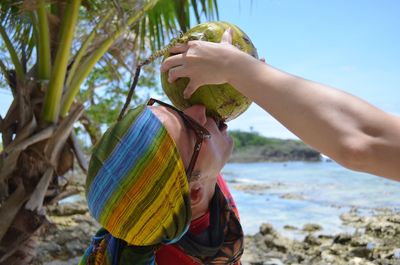 Close-up of man holding tree at beach against sky