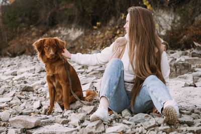 Young woman and dog retriever walks on river shore at autumn season