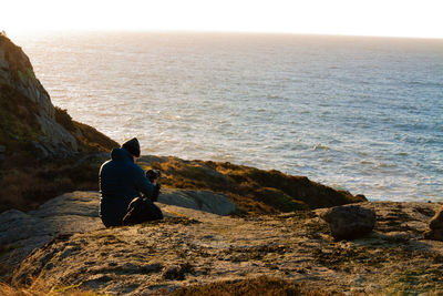 Rear view of man sitting on rock by sea